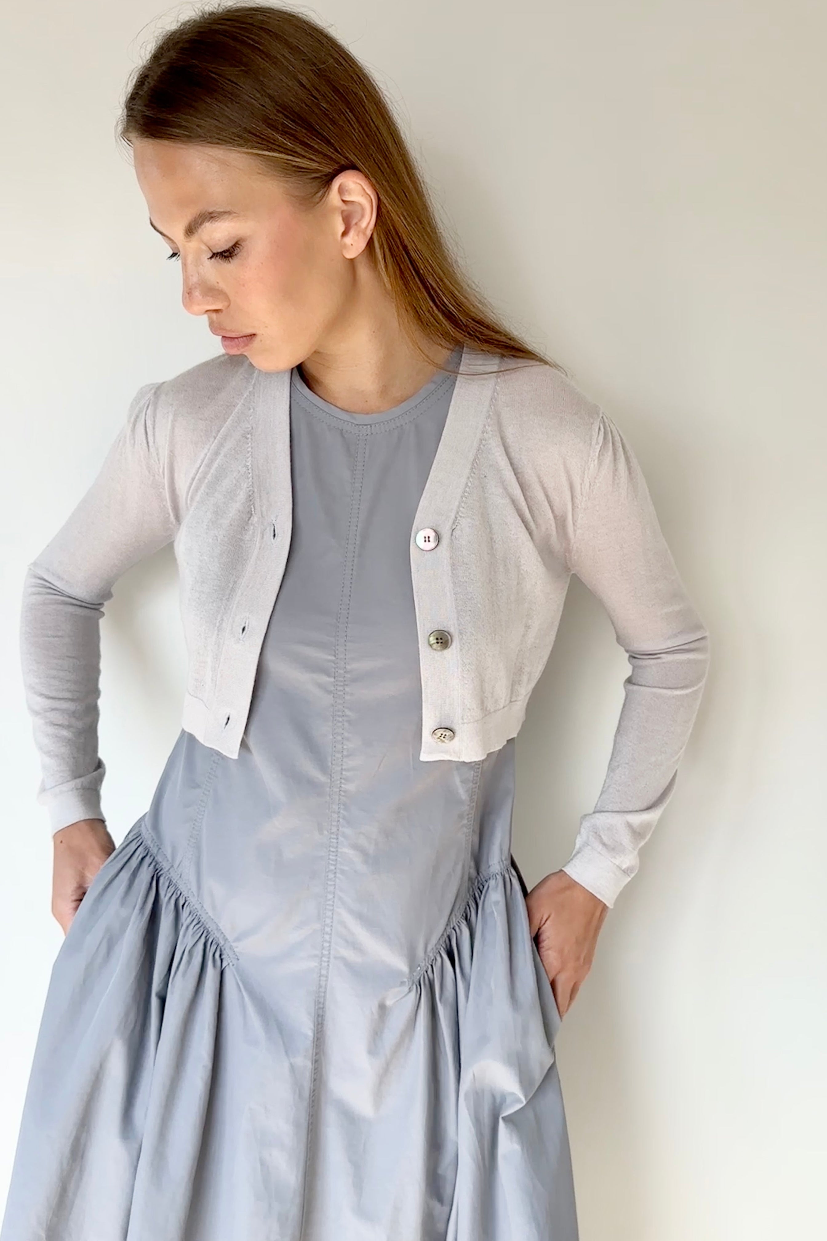 Woman wearing a light gray cardigan over a blue dress against a white background