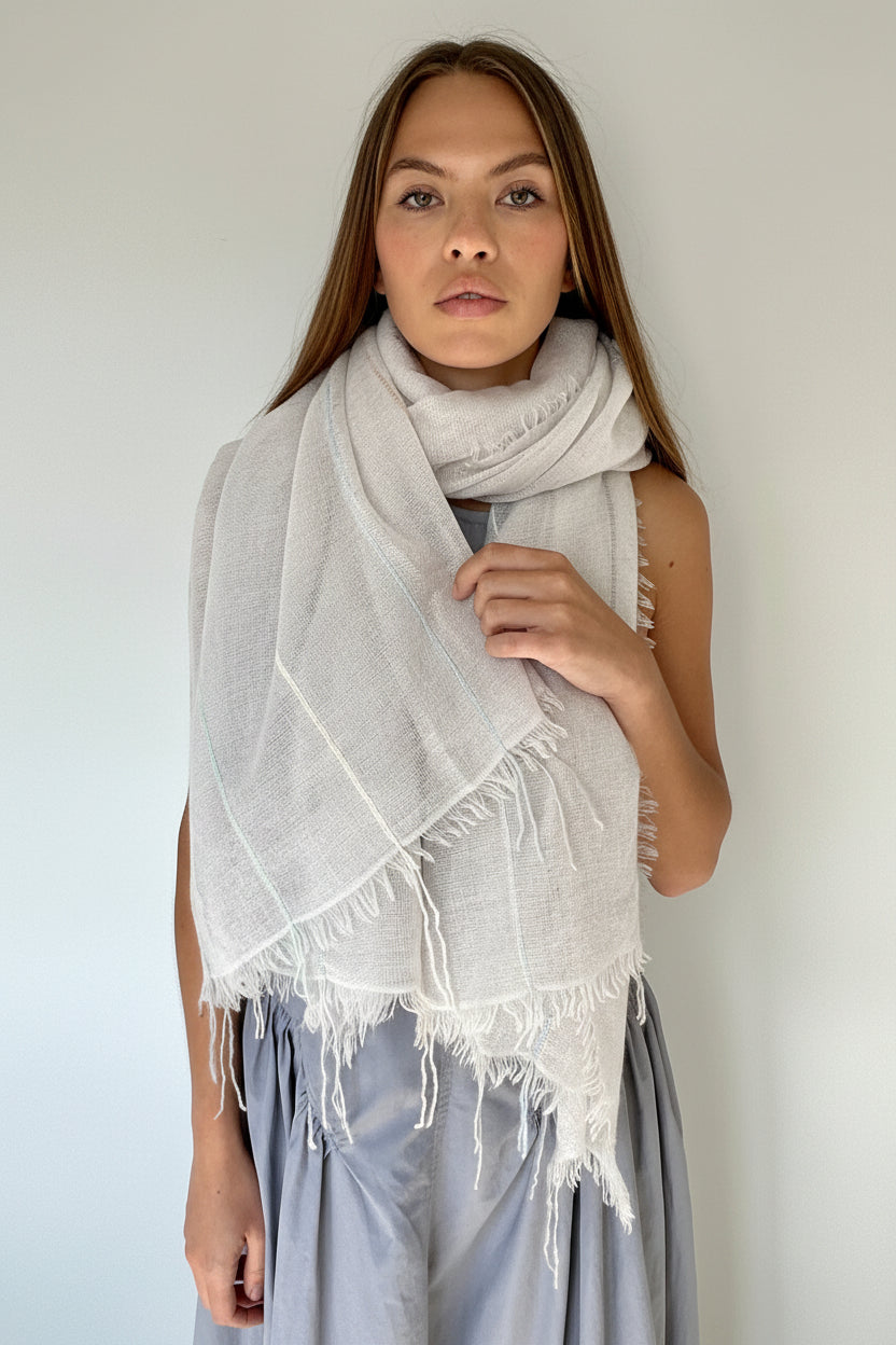 Woman wearing a light gray scarf with white fringe against a plain background