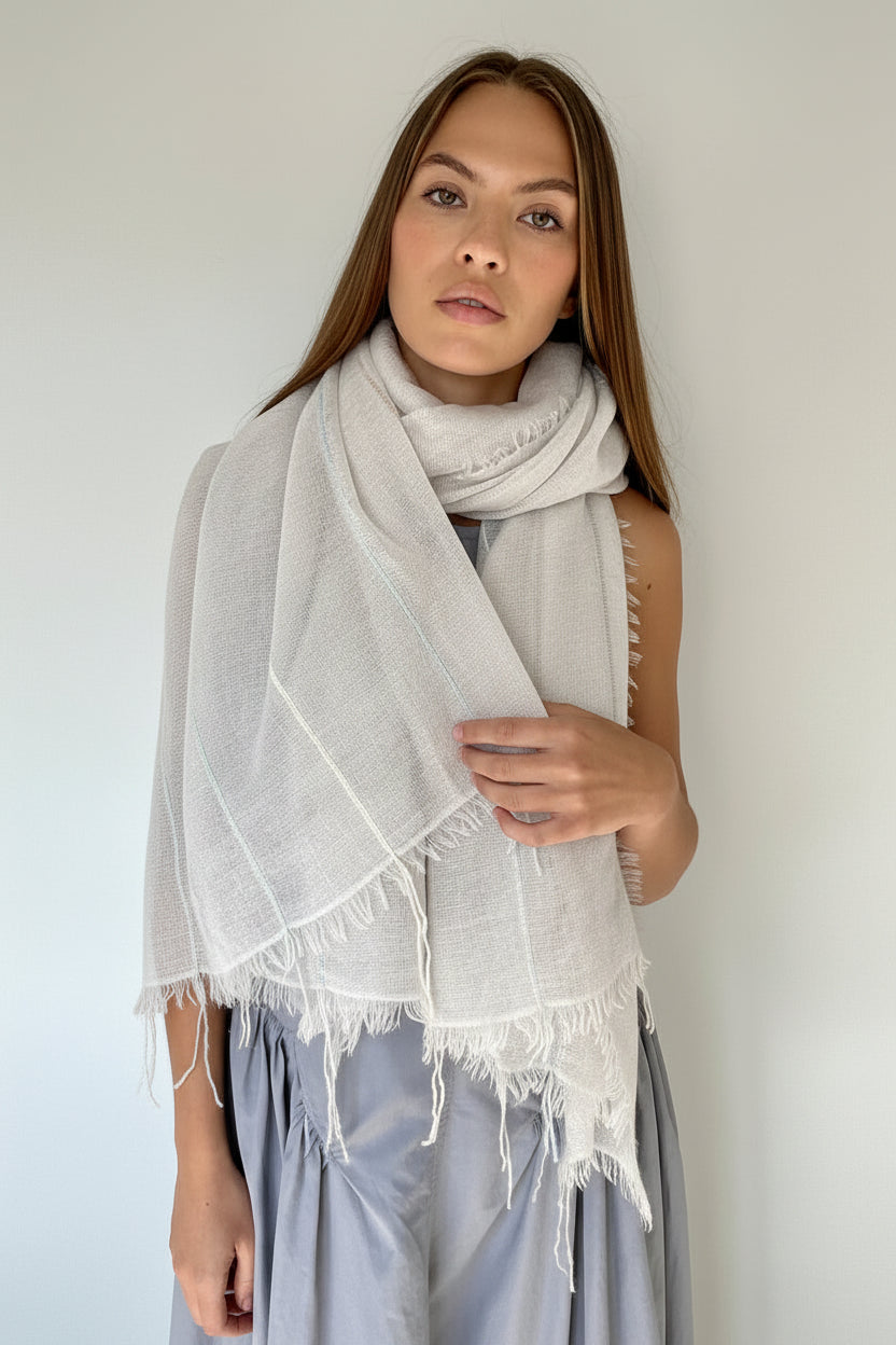Woman wearing a light gray scarf with white fringe against a plain background
