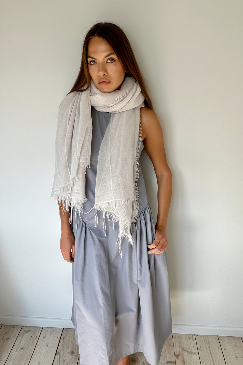 Woman wearing a light gray dress and scarf against a plain wall.