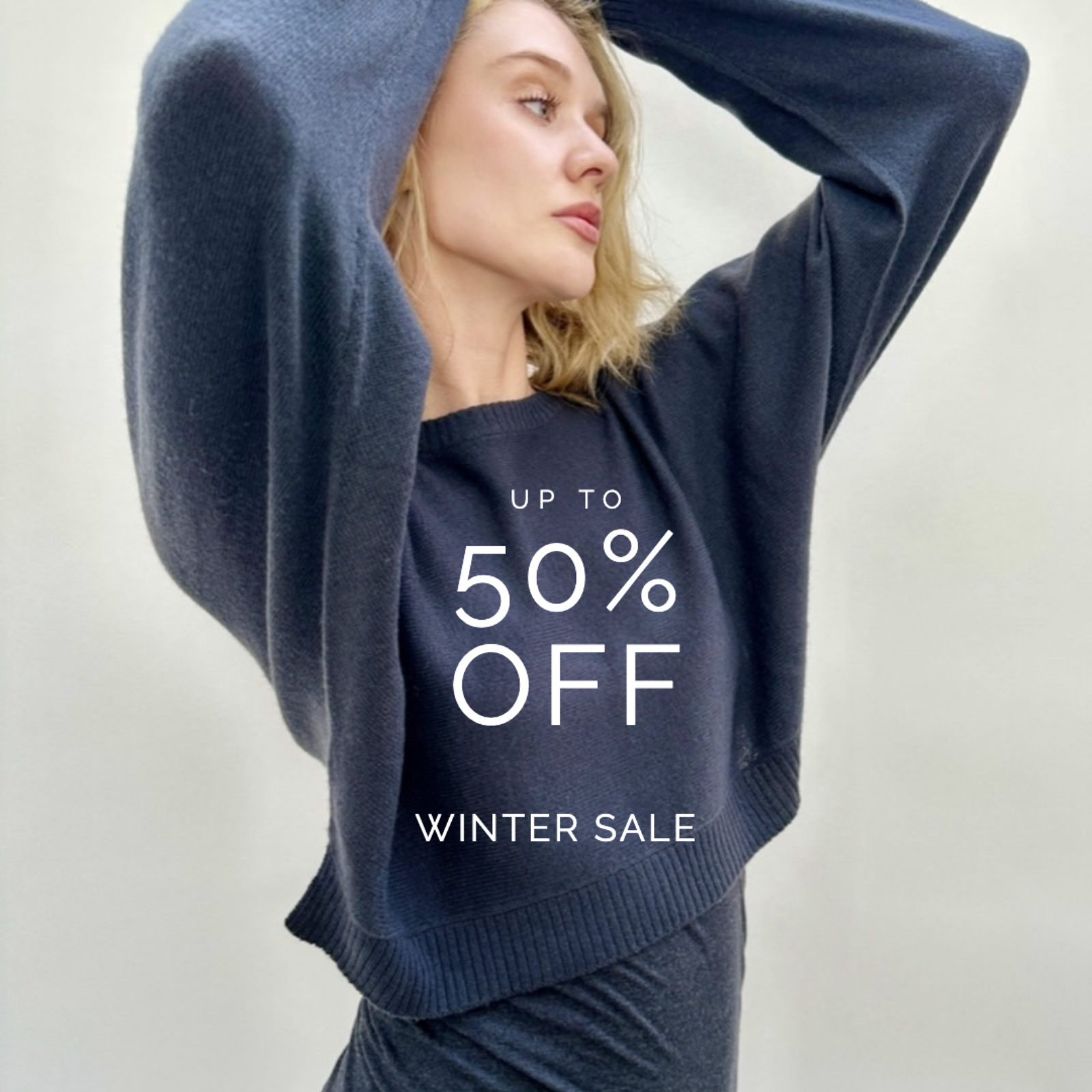 Woman wearing a navy sweater with 'Up to 50% Off Winter Sale' text on a plain background