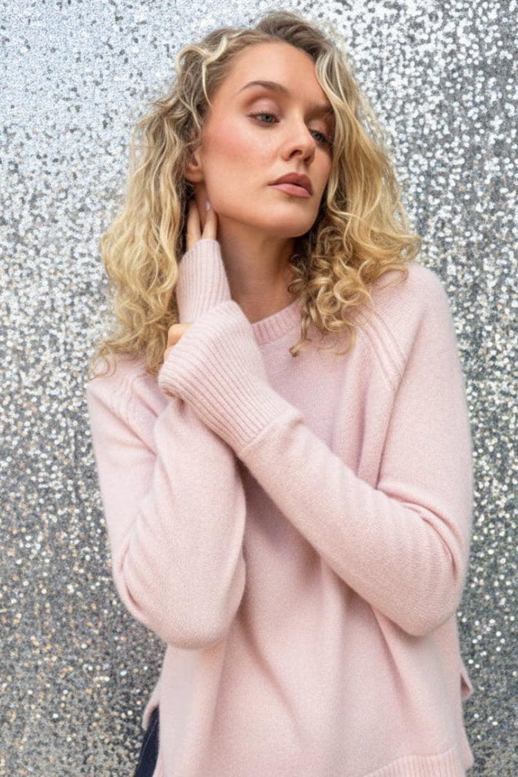 model in pale pink sweater against a silver wall
