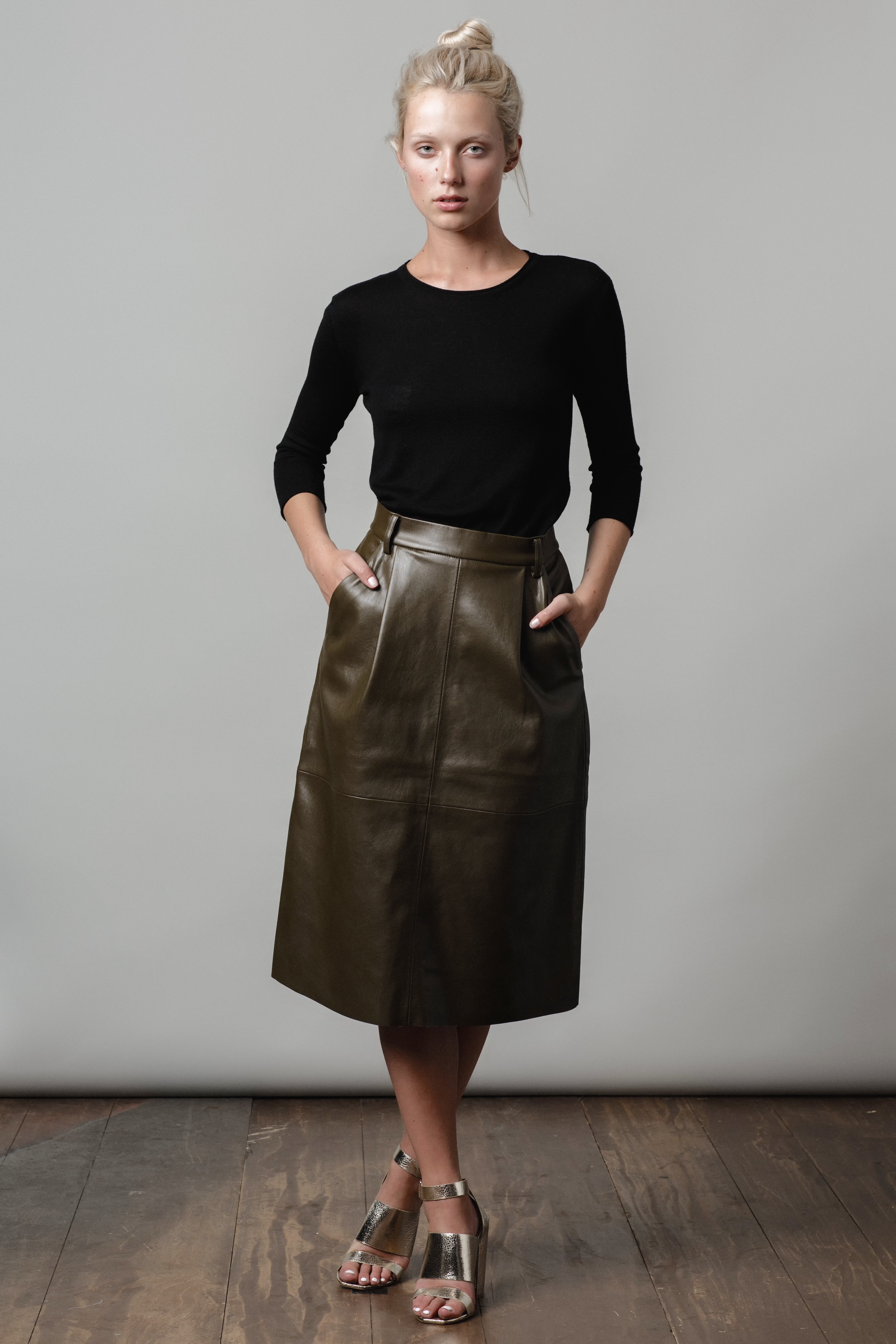 Woman wearing a black top and green leather skirt against a plain background