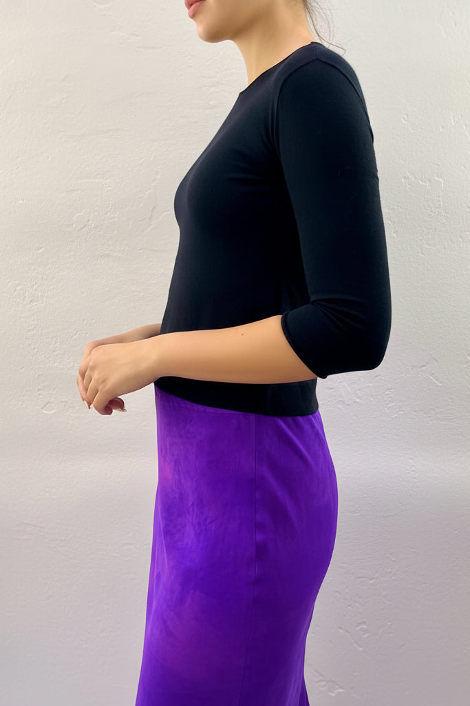 Model wearing a black cashmere silktop and purple skirt against a plain background
