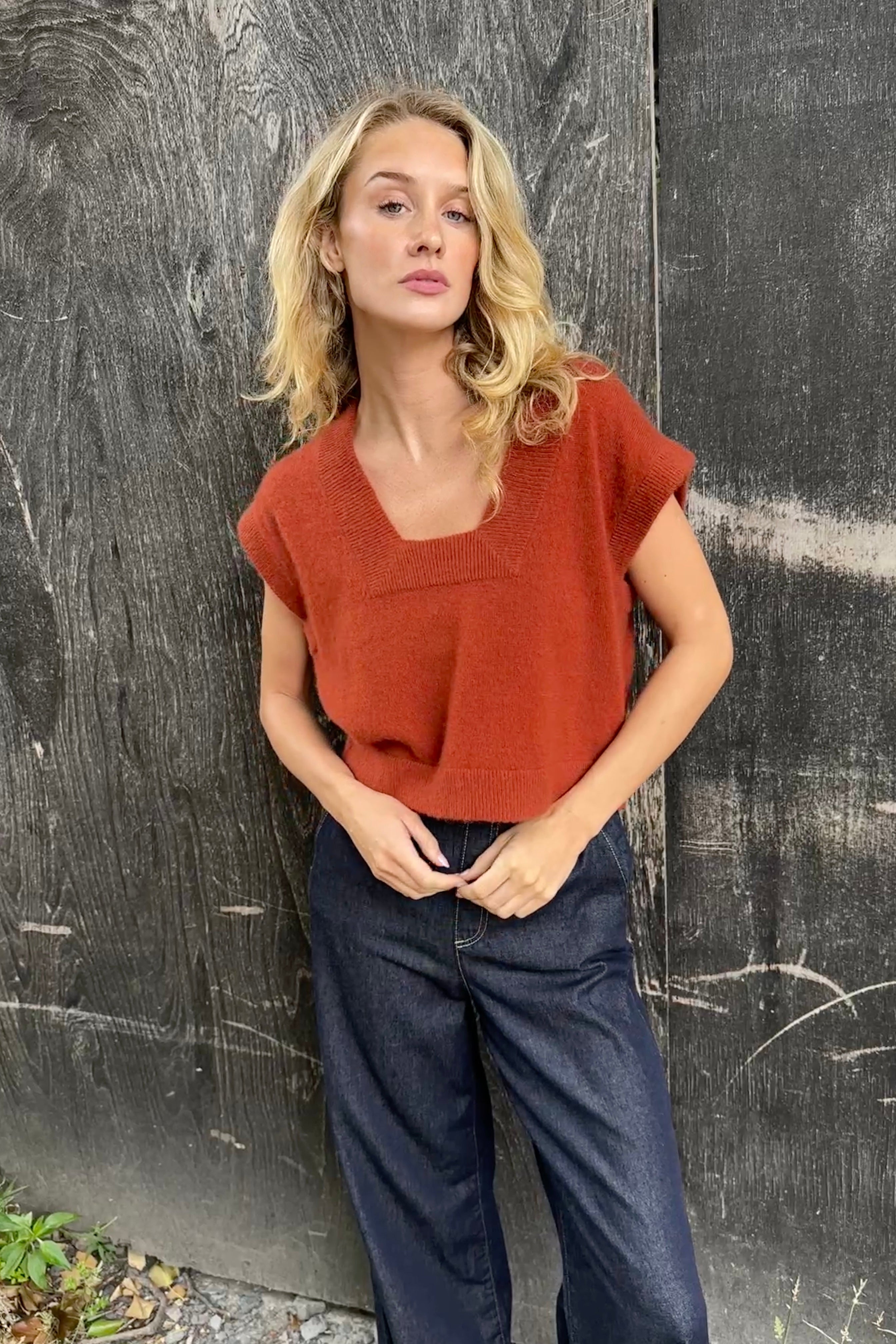 model wearing a rust-colored cashmere square neck knit tank top against a dark background