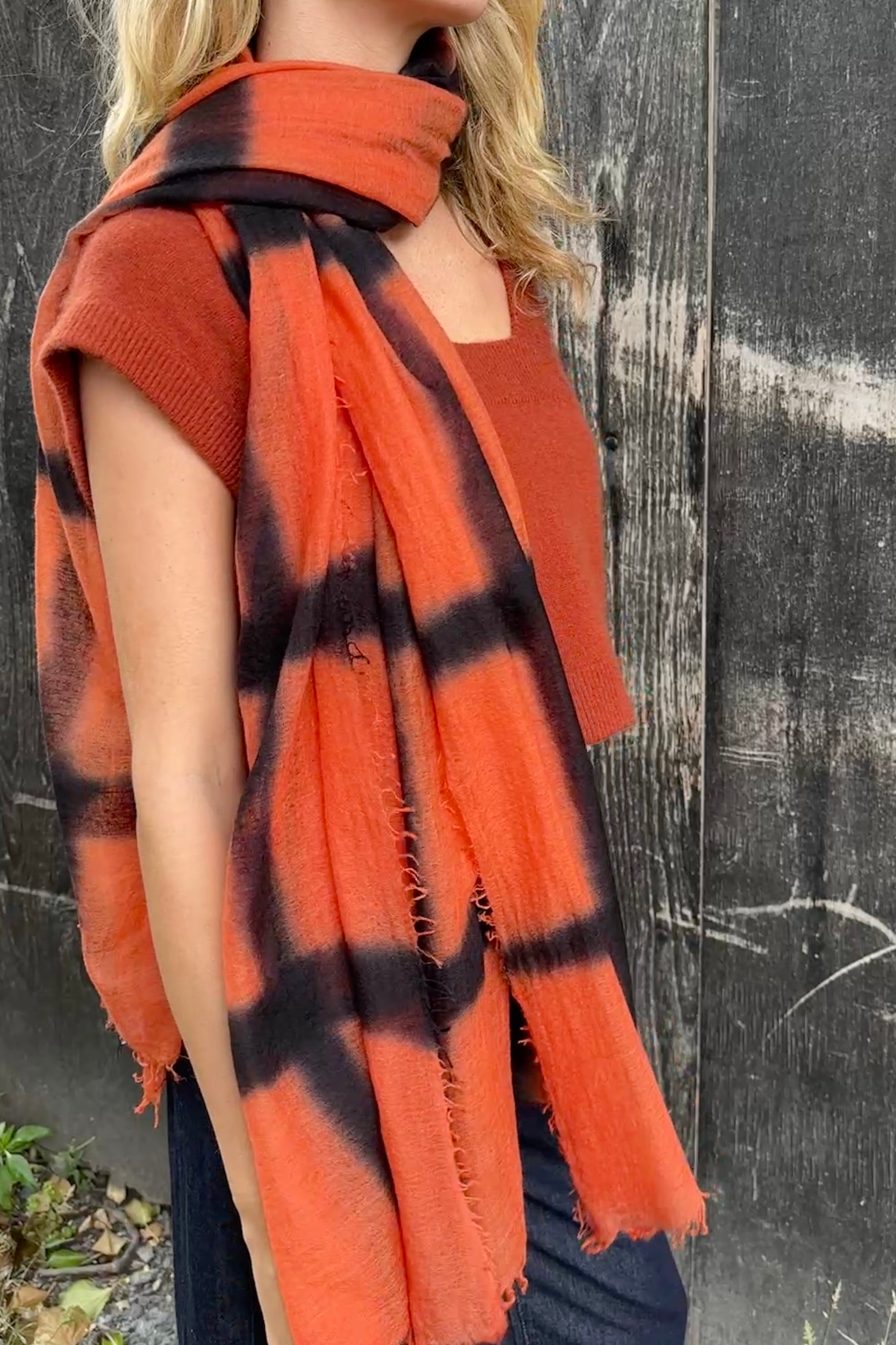 model wearing an orange and black stripe shibori tie dye scarf against a textured black background side view