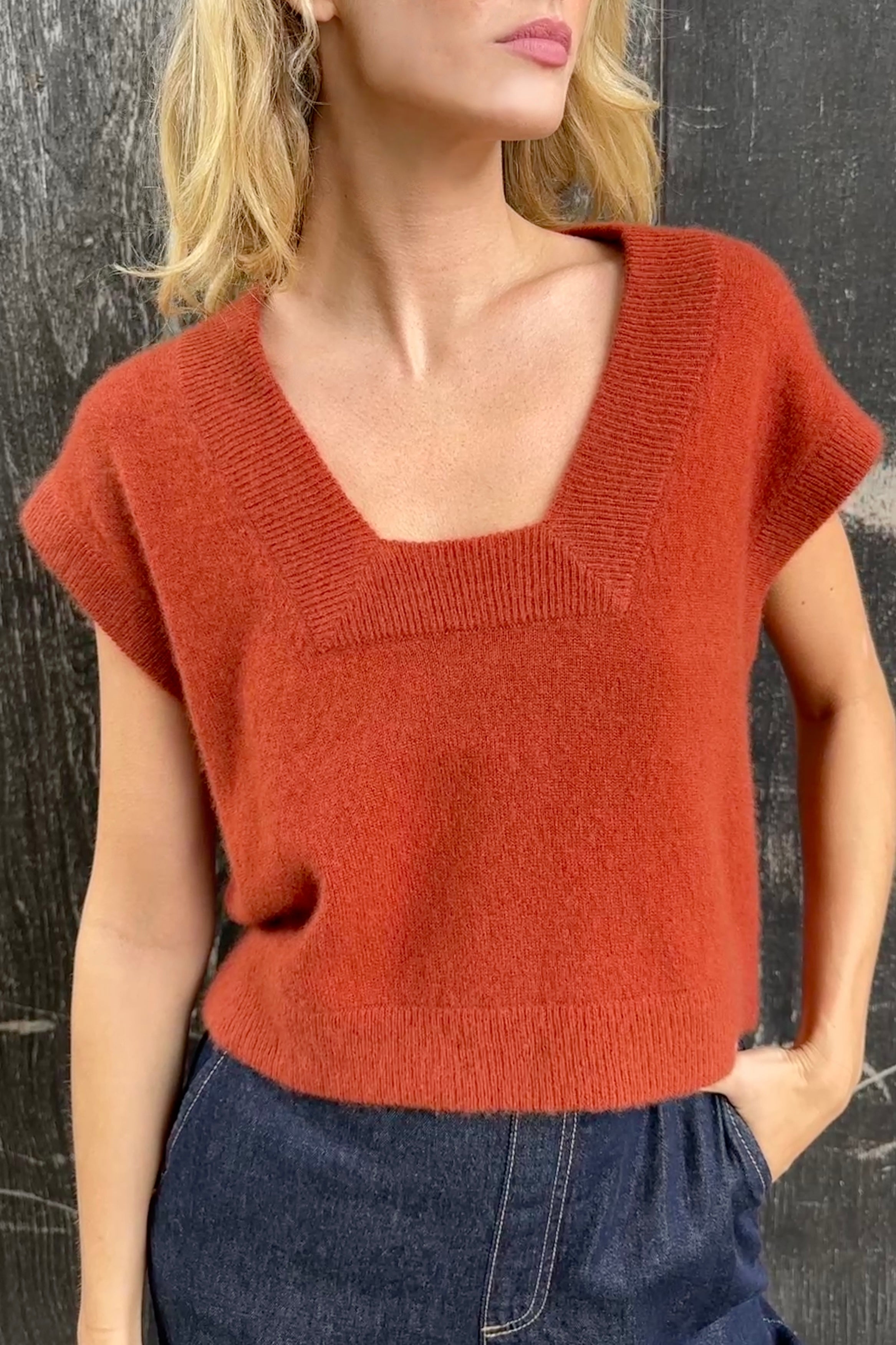 model wearing a rust-colored cashmere square neck knit tank top against a dark background