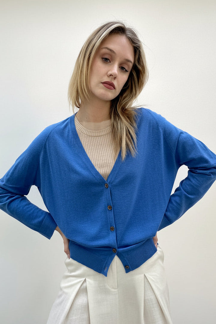 Woman wearing a blue cardigan over a beige sweater on a plain background
