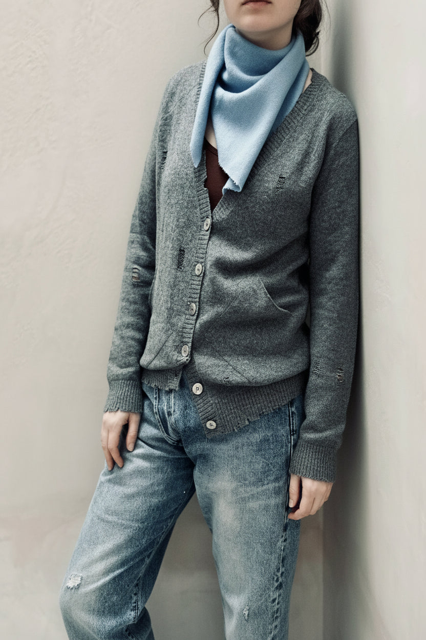 Person wearing a gray cardigan, light blue scarf, and distressed jeans against a plain background