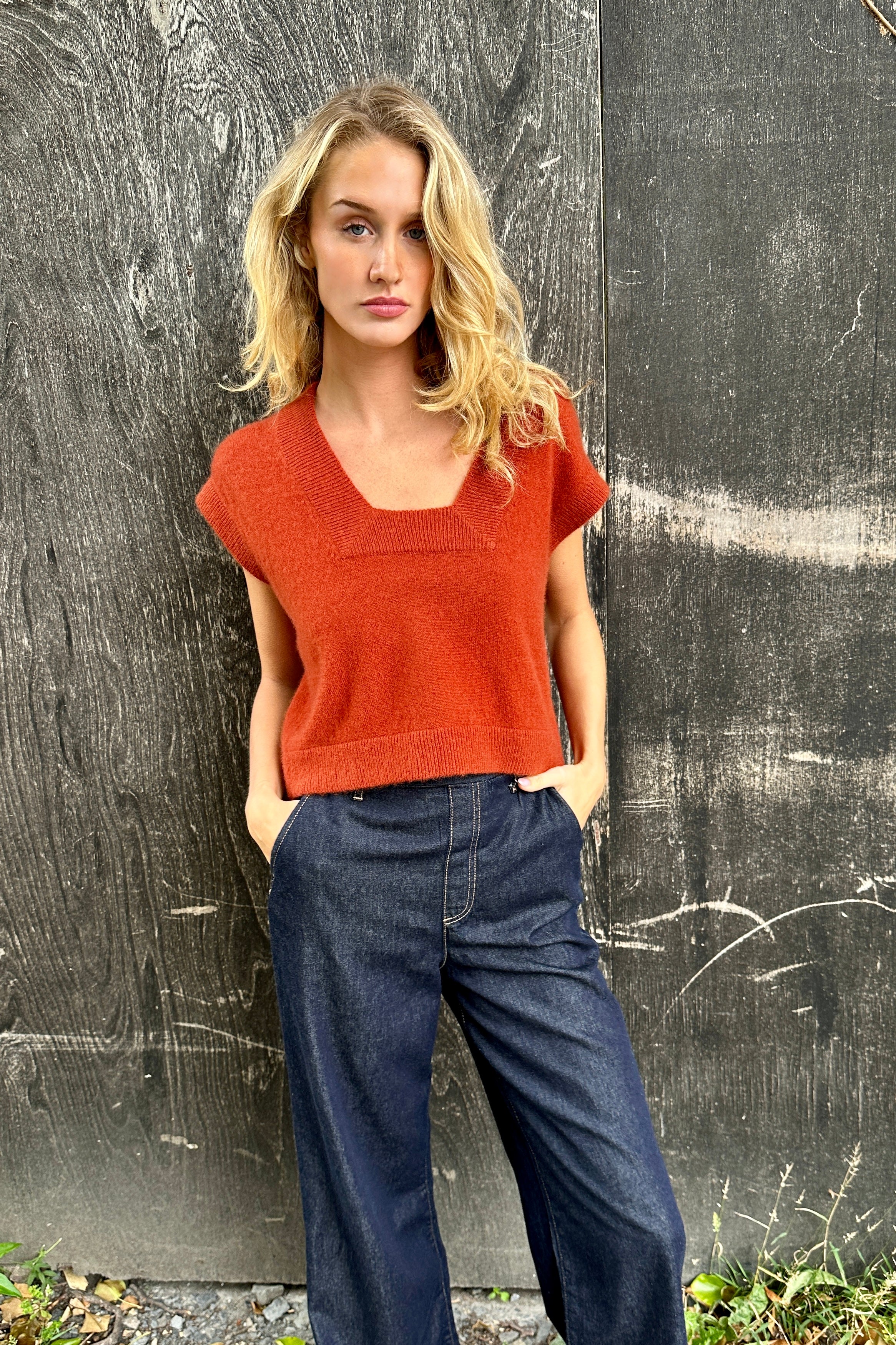 model wearing a rust-colored cashmere square neck knit tank top against a dark background