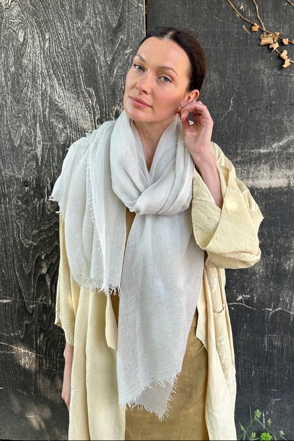Woman wearing a light-colored scarf against a textured wall.