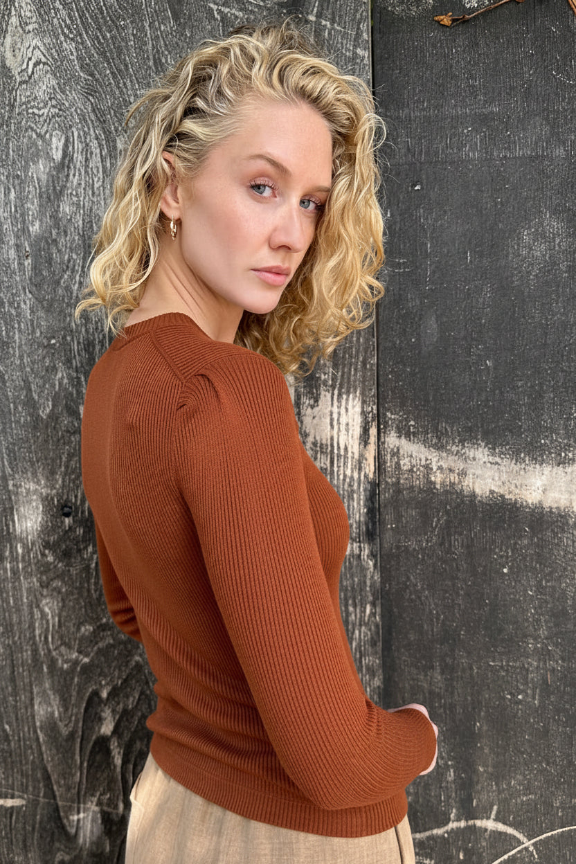 Woman wearing a brown sweater against a textured black wall