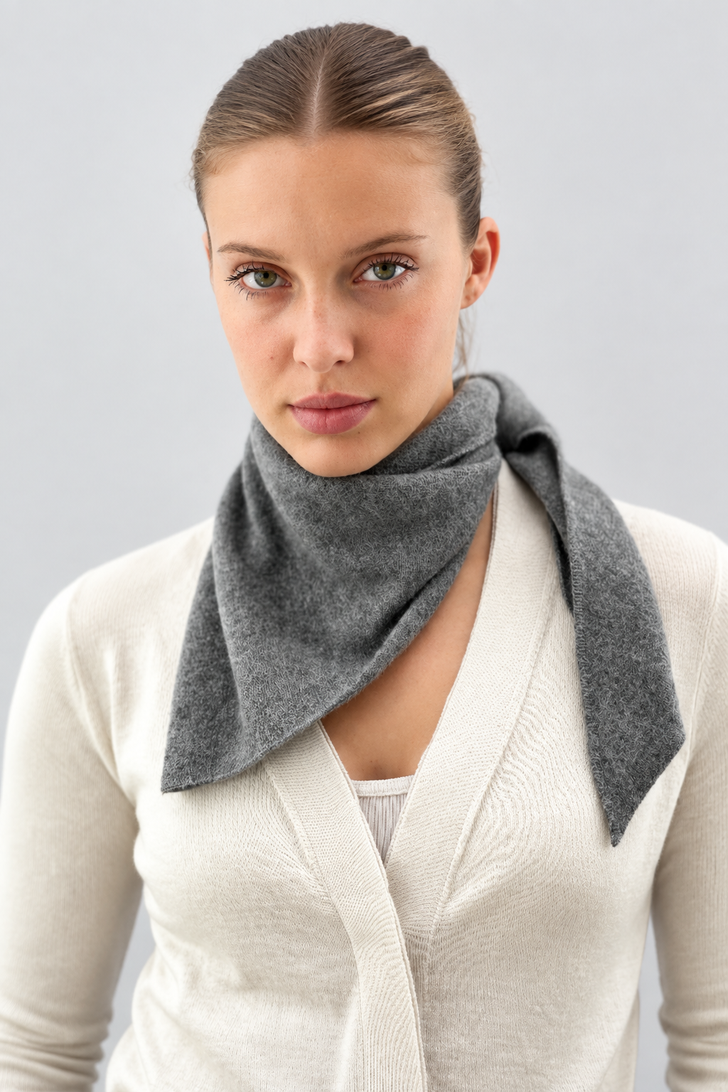 A close-up of a woman wearing a gray knit neck warmer or cowl layered under a cream-colored cardigan, set against a plain light gray background.