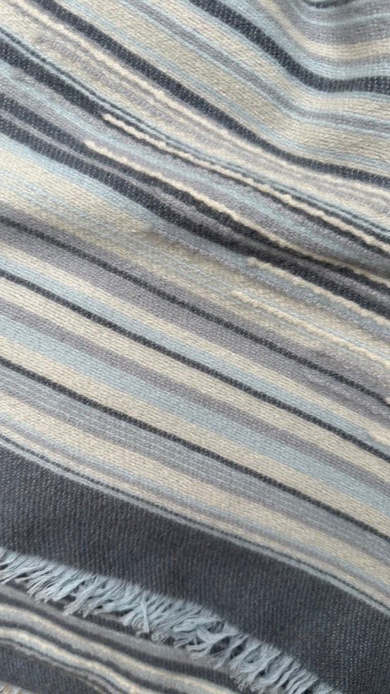 Close-up of a striped fabric with wavy pattern in  pale blue,grey, gray, black, and beige. Mizzy stripe blues cream scarf swatch