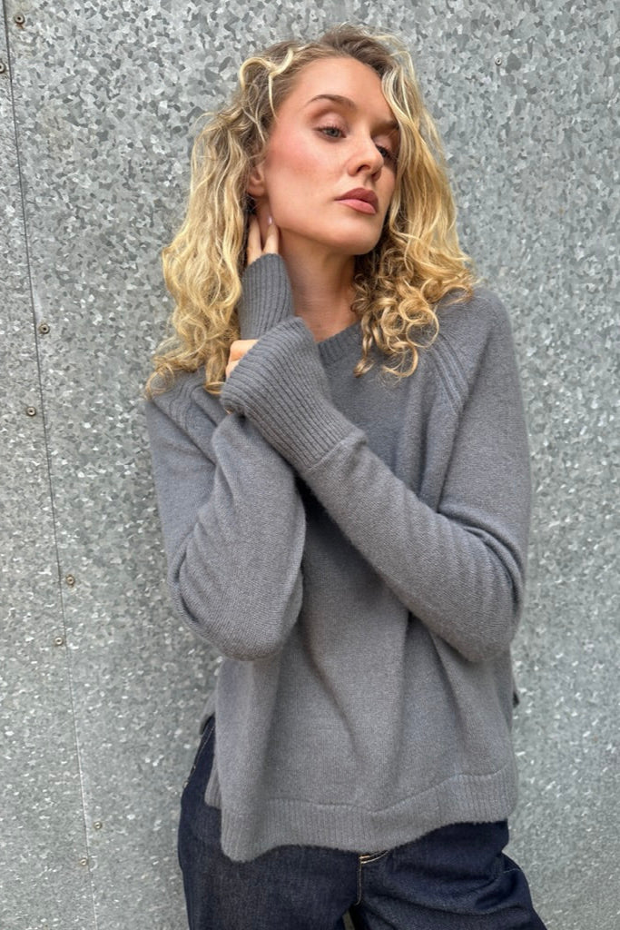 Woman wearing a gray  cashmere sweater against a textured gray wall