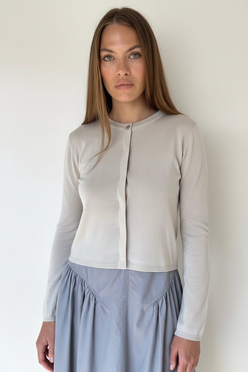 Woman wearing a light gray cardigan over a white shirt with a blue skirt against a plain background