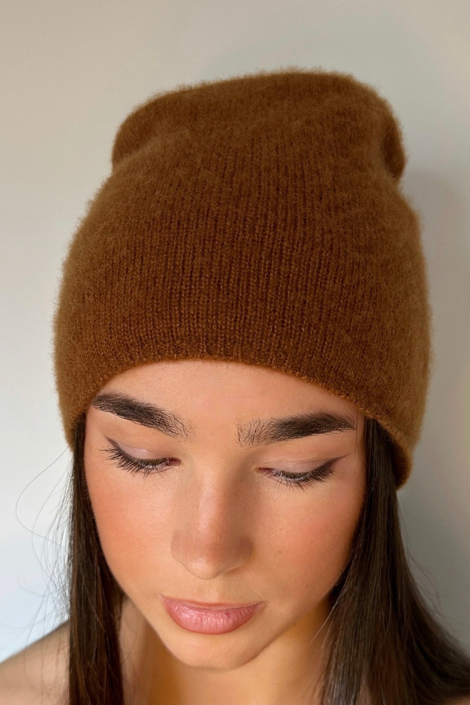 Woman wearing a  beety brown knit cashmere silkl beanie against a plain background
