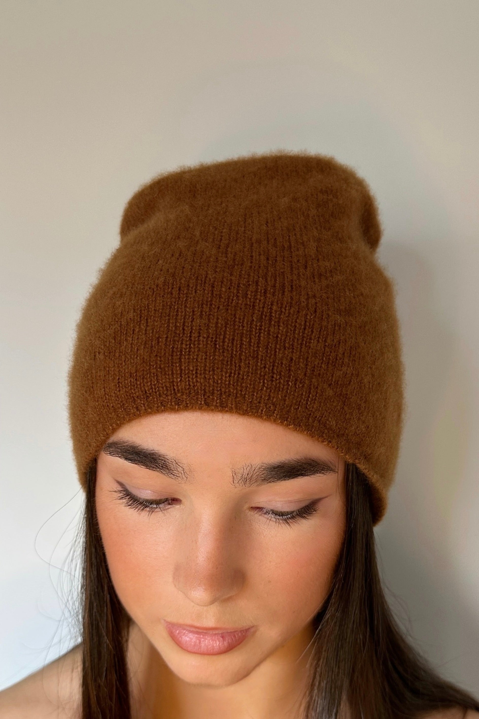 Woman wearing a  beety brown knit cashmere silkl beanie against a plain background