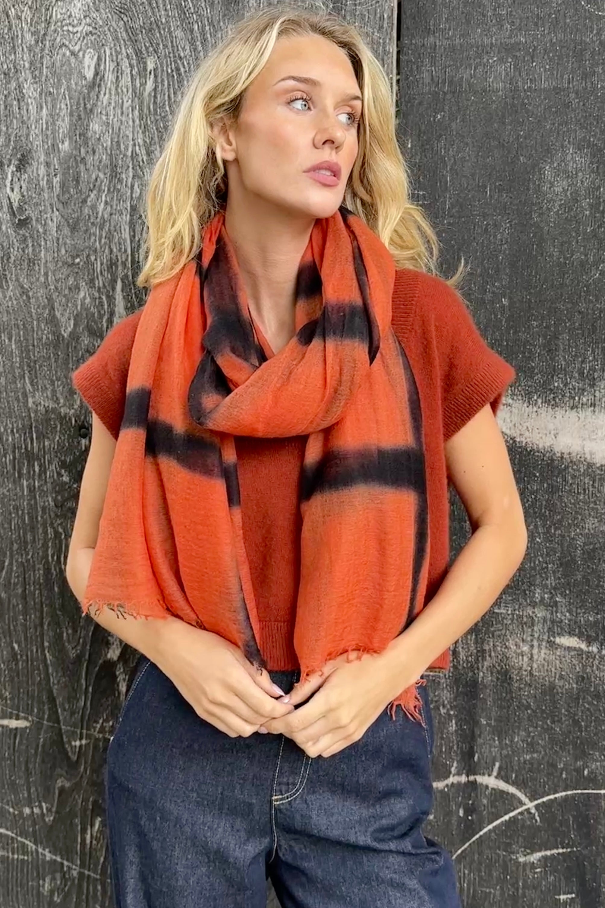 model wearing an orange and black stripe shibori tie dye scarf against a textured black background