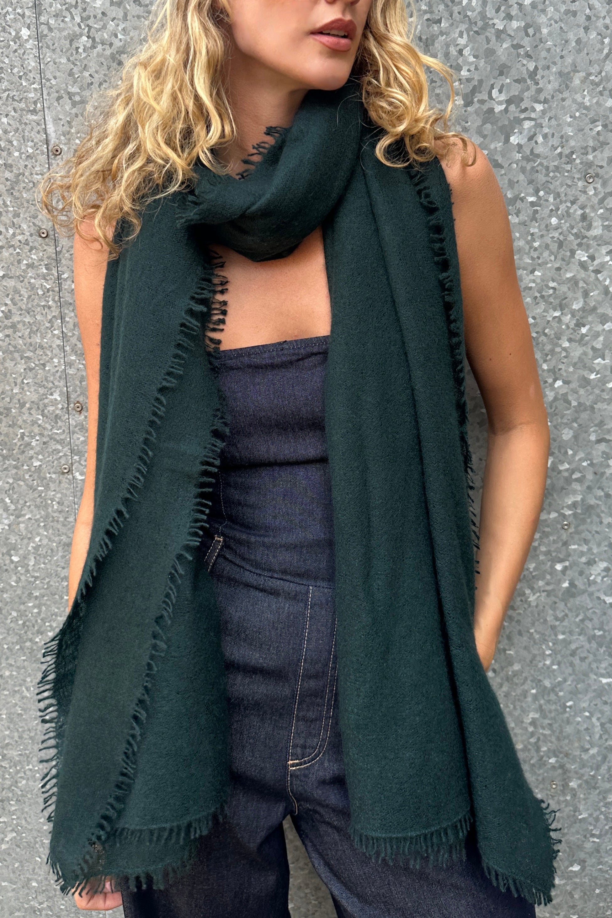 model wearing a dark green eighty cashmere  scarf  with fringe against a gray background