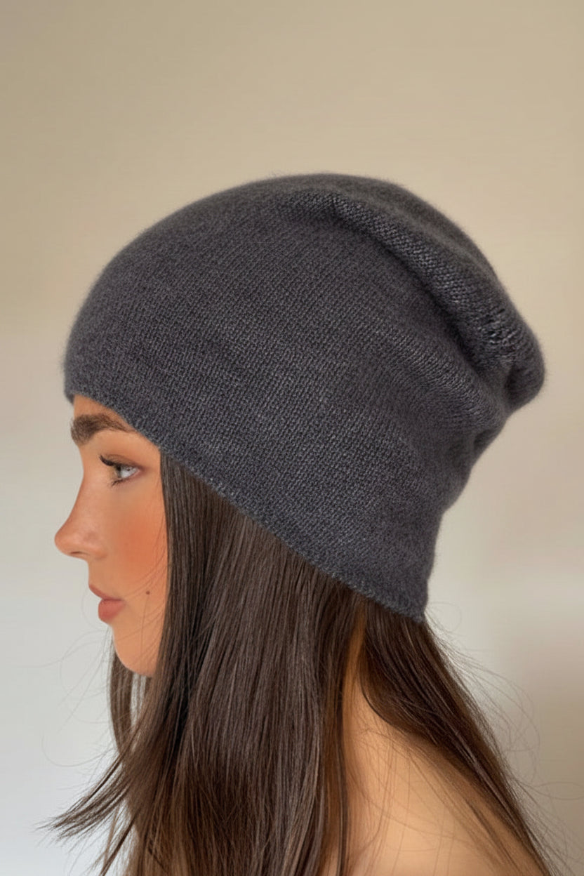 A woman shown in profile wearing a dark gray knit slouchy beanie against a plain off-white wall.