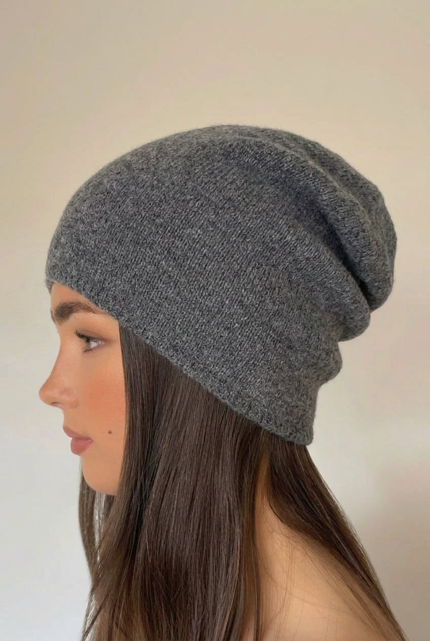 A woman shown in profile wearing a dark gray knit slouchy beanie against a plain off-white wall.