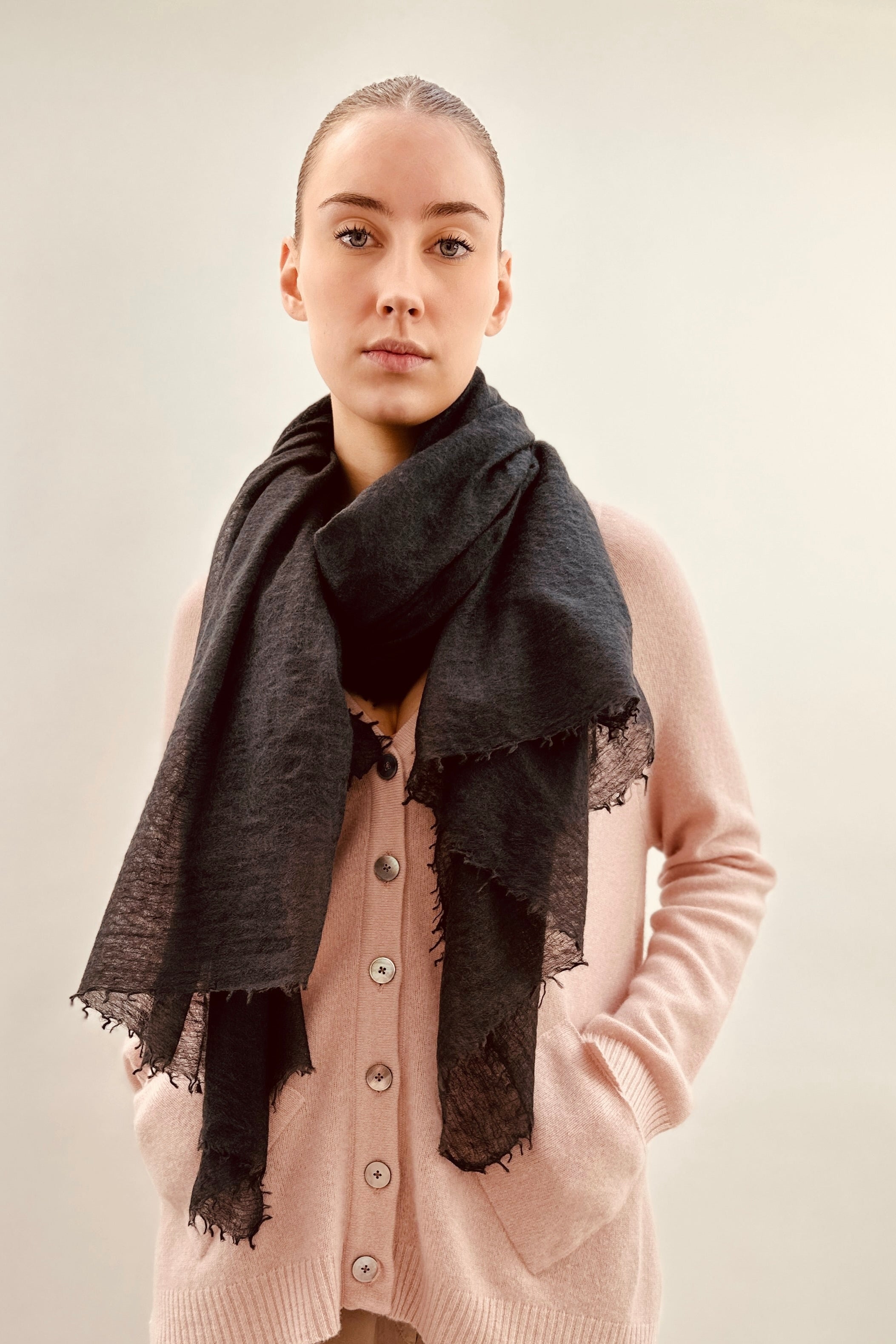 Woman wearing a pink cardigan and black scarf against a plain background