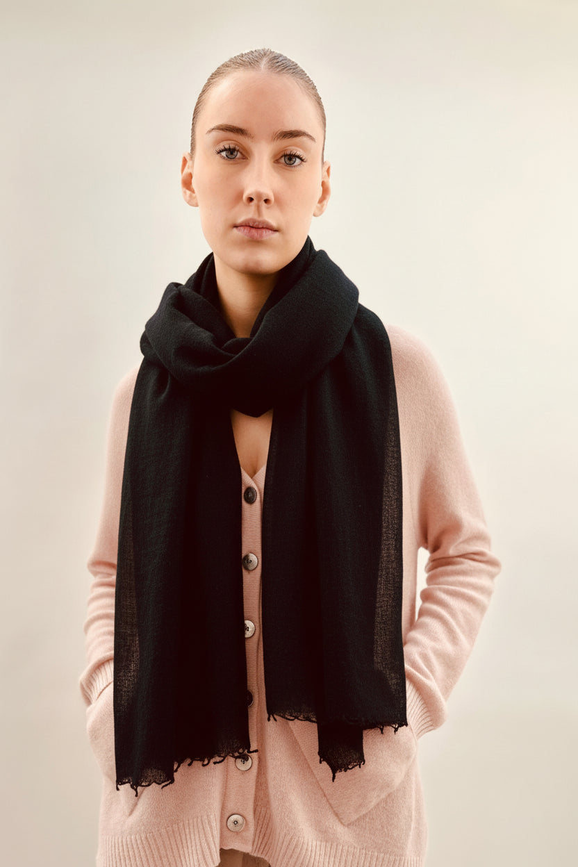 Woman wearing a pink cardigan and black scarf against a plain background