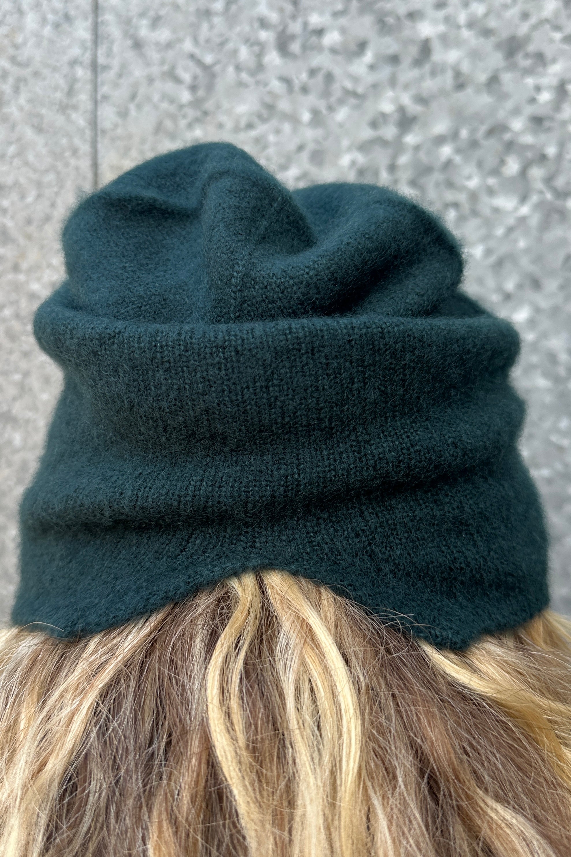 Dark teal blue knitted beanie on a person with a neutral background
