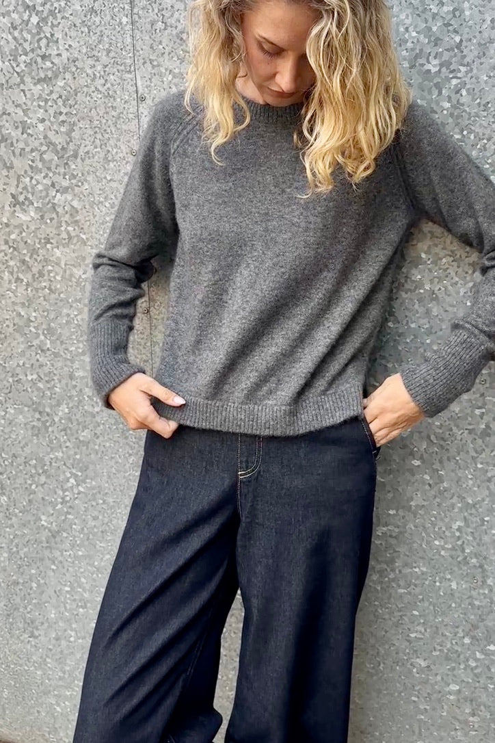 model wearing a gray  grey hethna cashmere sweater and dark jeans against a textured wall.