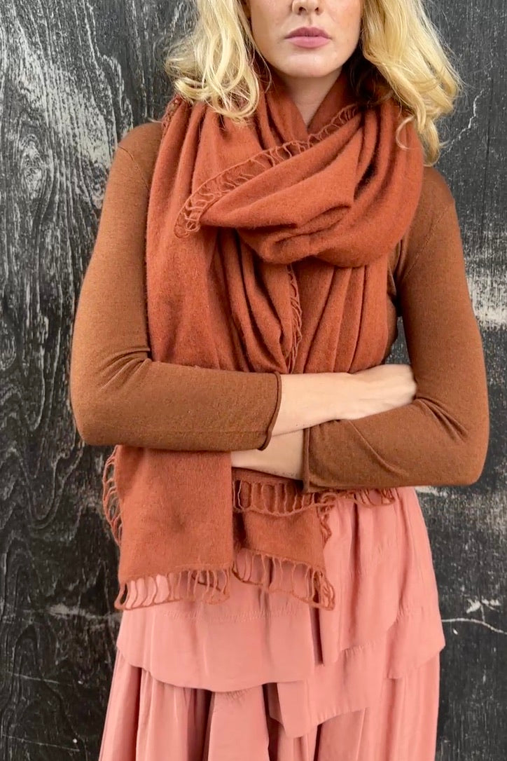 Woman wearing a rust-colored scarf and dress against a textured black background