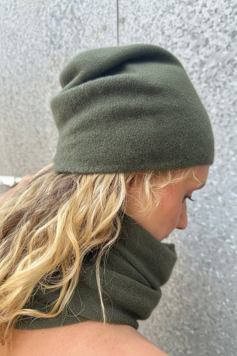 Model wearing a dark  teal blue beanie and matching scarf against a textured wall.