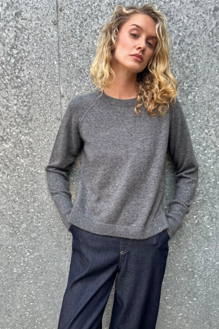 model wearing a gray  grey hethna cashmere sweater and dark jeans against a textured wall.
