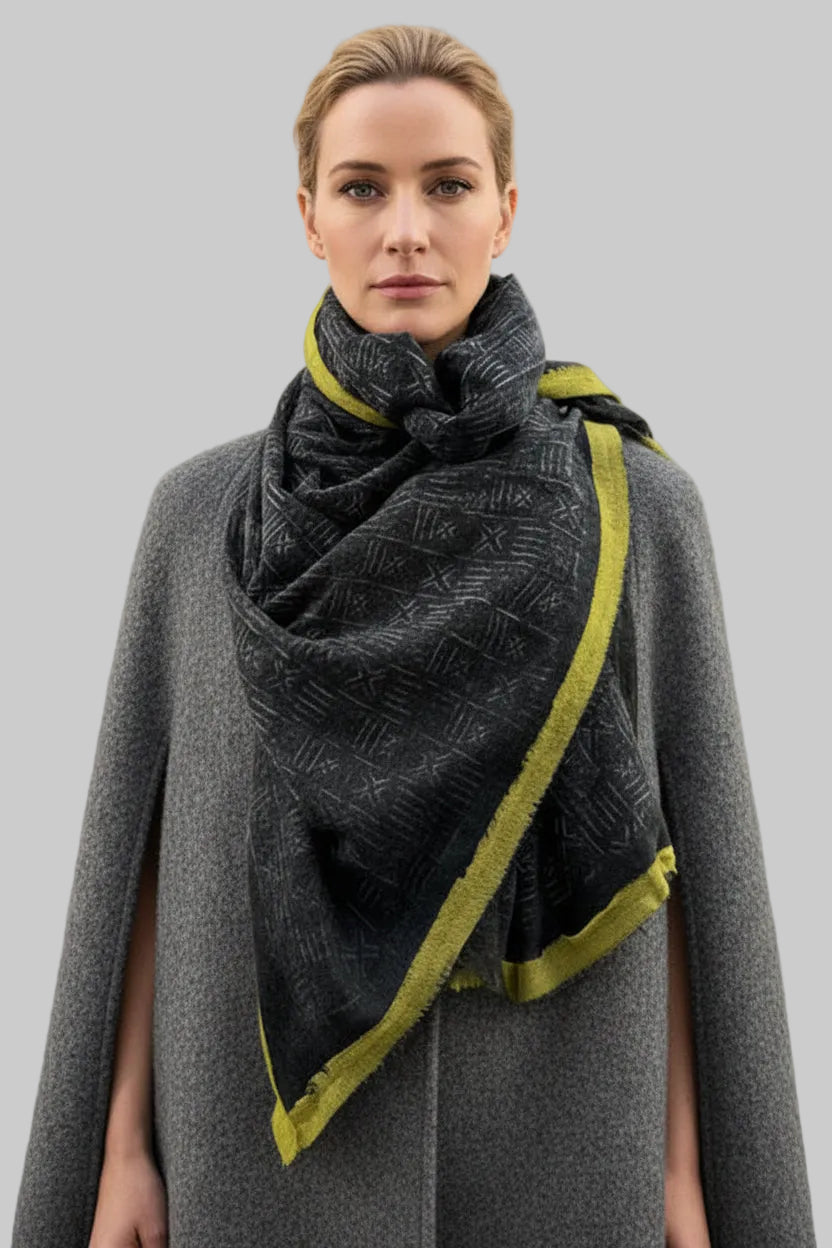 model against a linen wall in a print scarf and grey coat