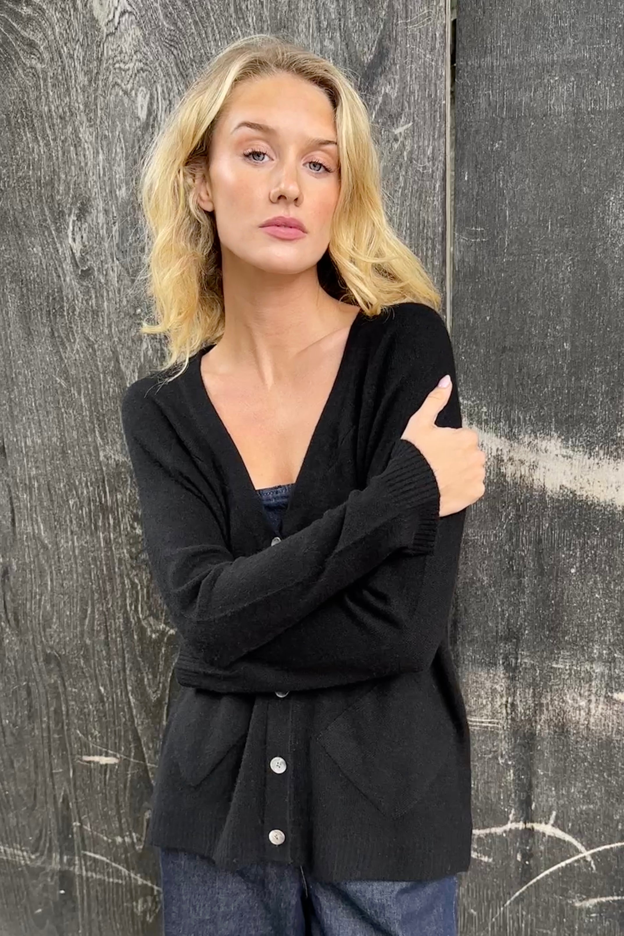 Woman wearing a black cashmere zola cardigan against a textured gray wall