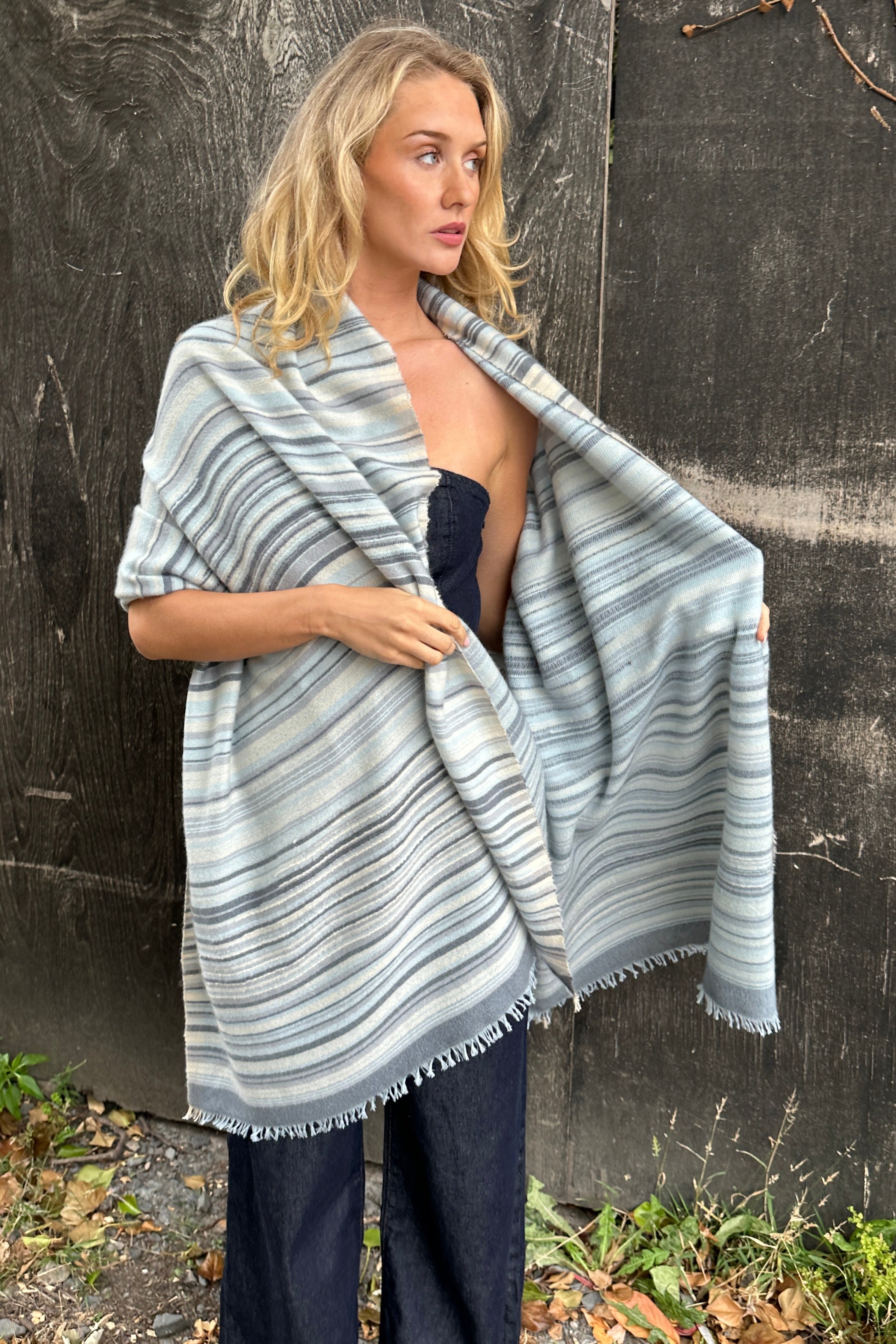 Mizzy stripe blues cream scarf wearing a striped shawl against a dark wall.