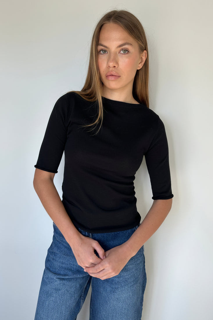 Woman wearing a black top and blue jeans against a white background