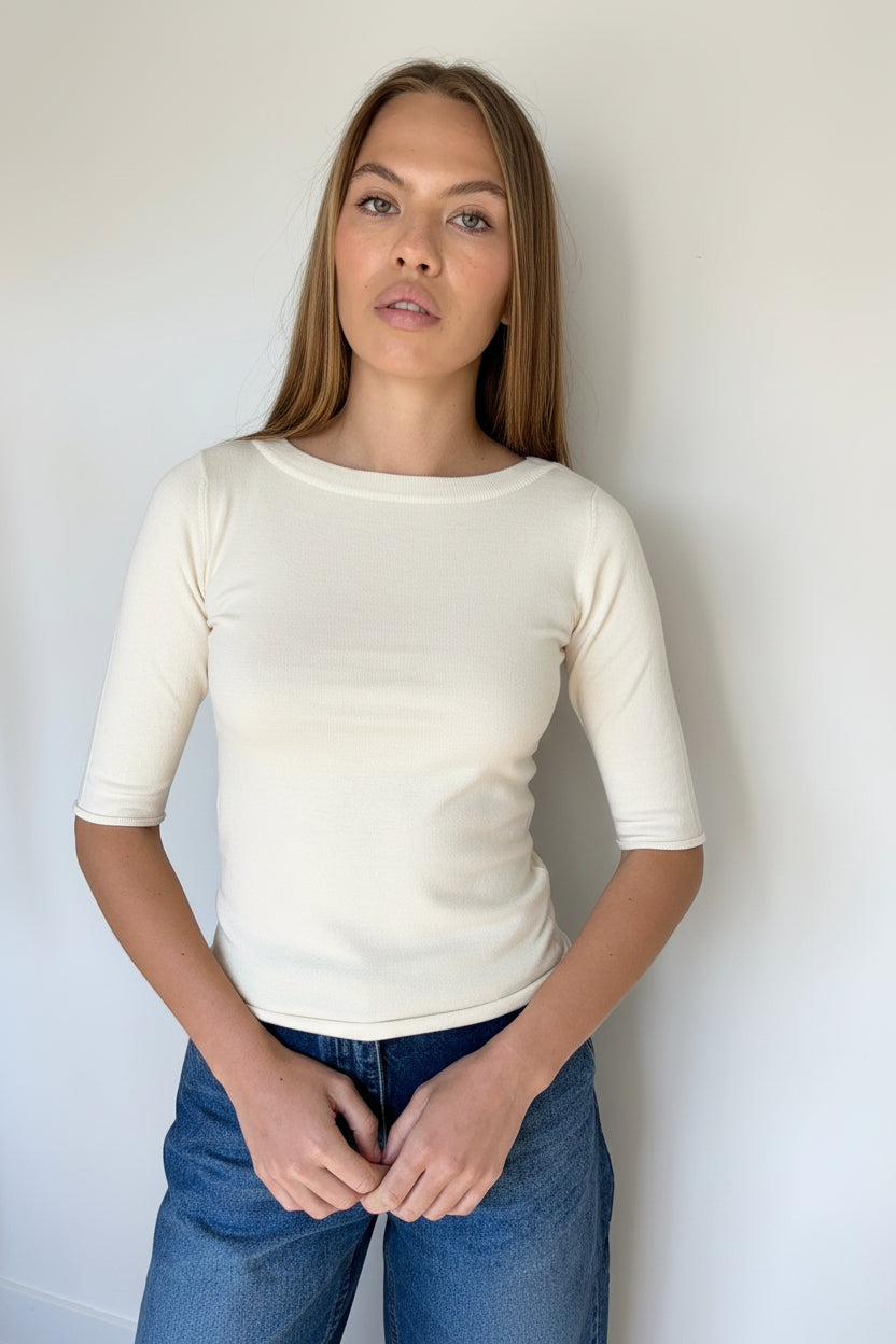 Woman wearing aivory r shirt and blue jeans against a plain background