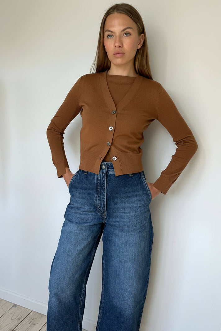 Person wearing a brown cardigan and blue jeans on a white background