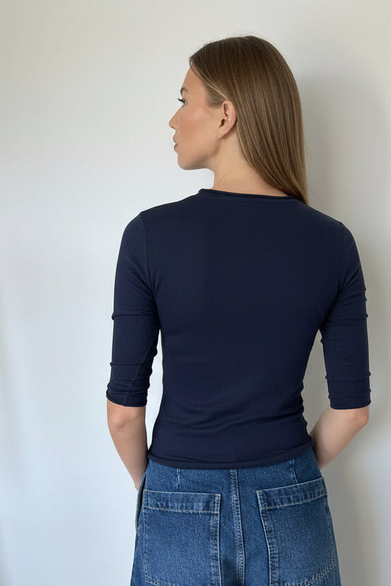Person wearing a navy blue long-sleeve top and blue jeans against a white wall.
