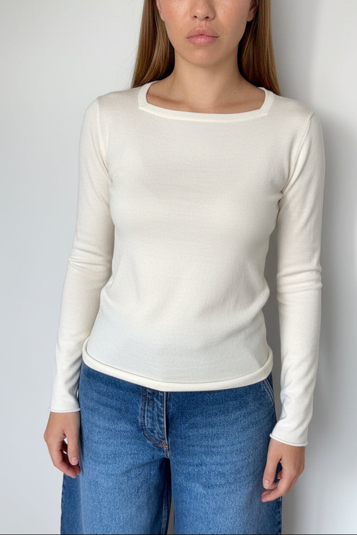 Woman wearing a off white long-sleeve top and jeans against a white background