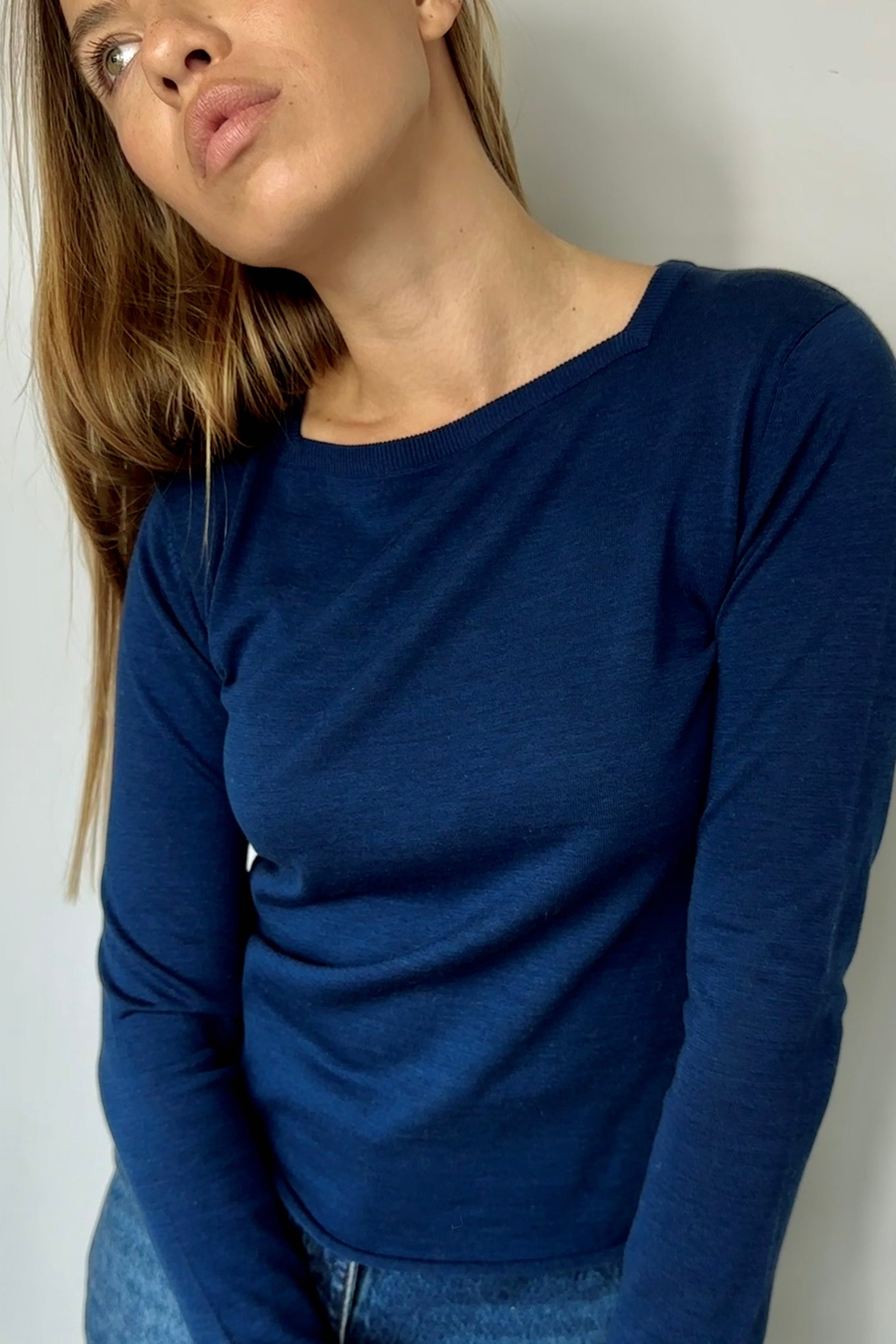 Woman wearing a blue long-sleeve top and jeans against a plain background