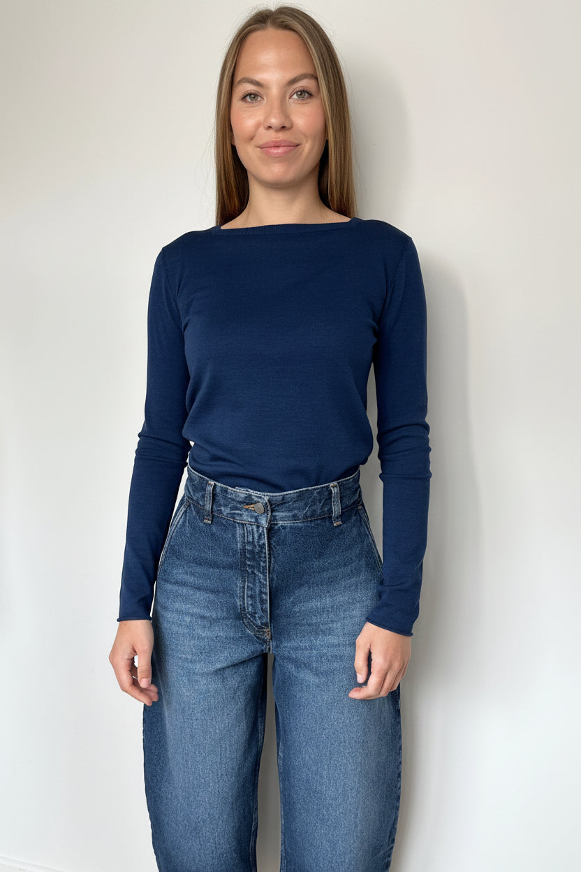 Woman wearing a navy long-sleeve top and blue jeans against a white background