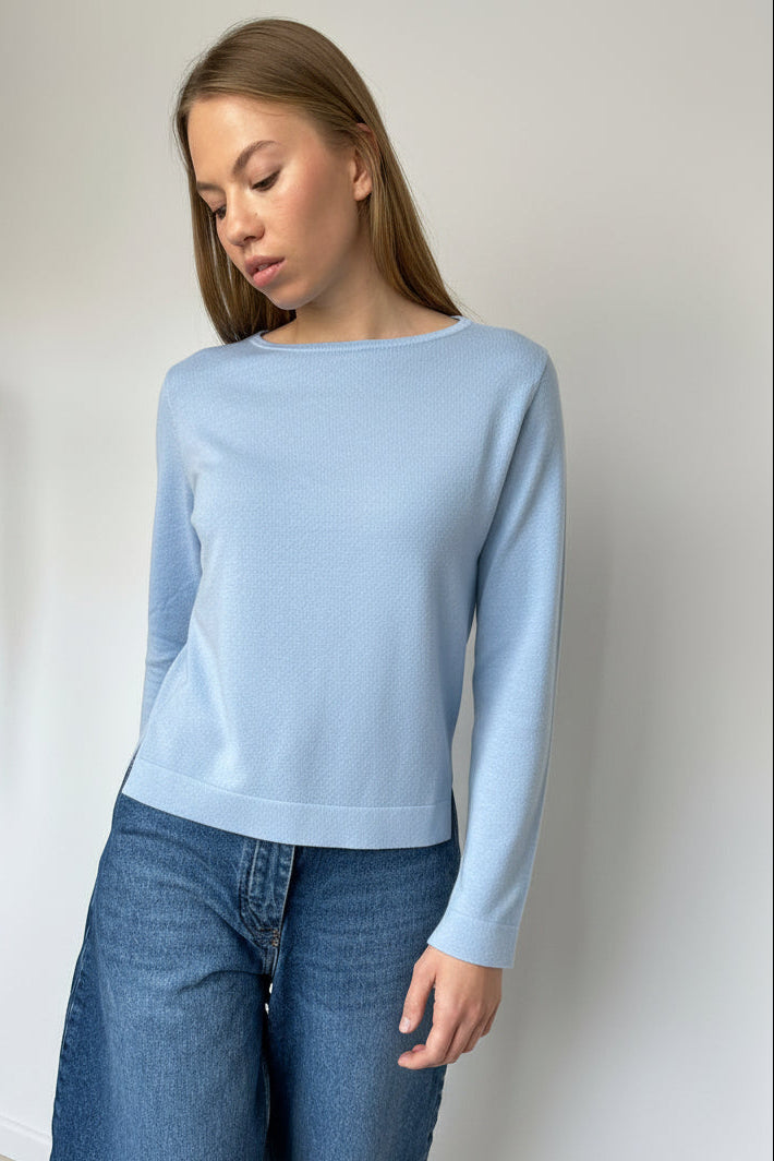 Woman wearing a dark green sweater and blue jeans against a plain background