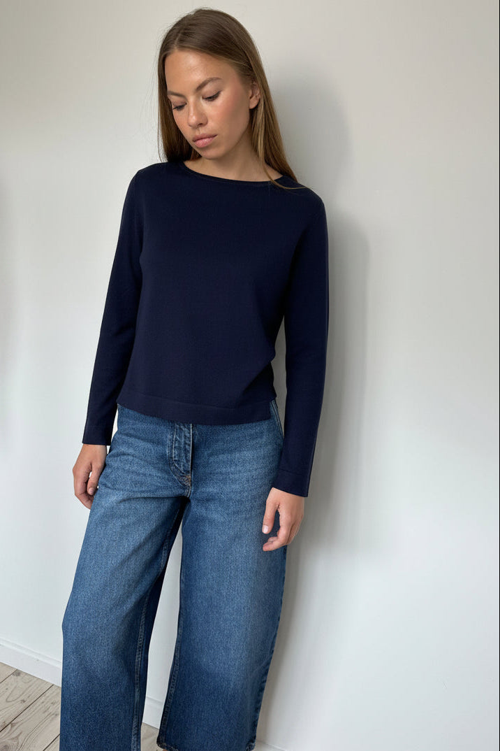 Woman wearing a navy sweater and blue jeans against a white wall