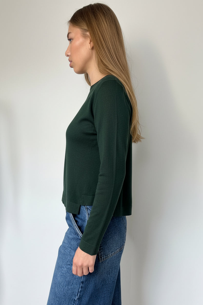 Person wearing a green long-sleeve top and blue jeans against a plain background