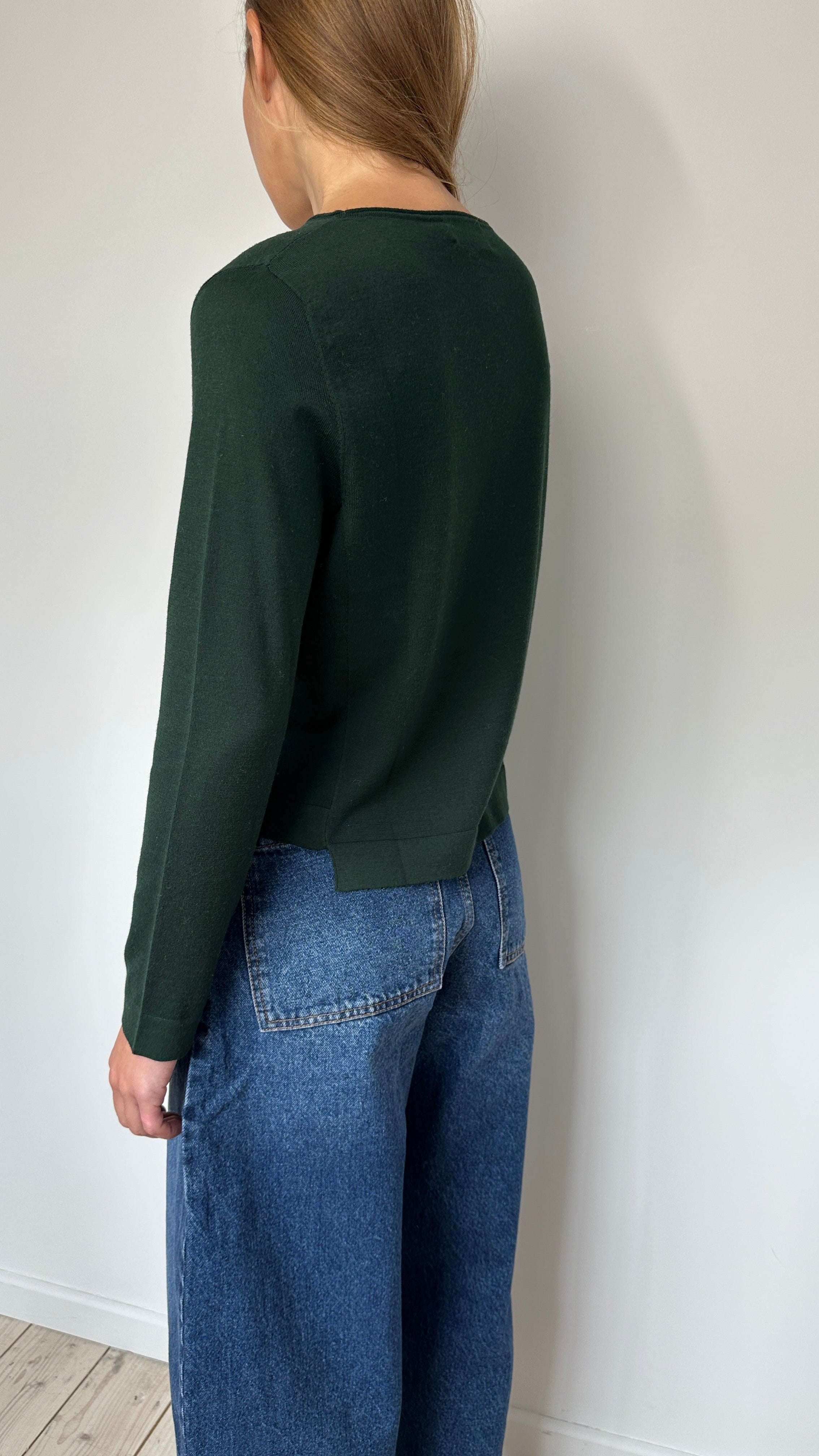 Person wearing a green  top and blue jeans on a white floor.