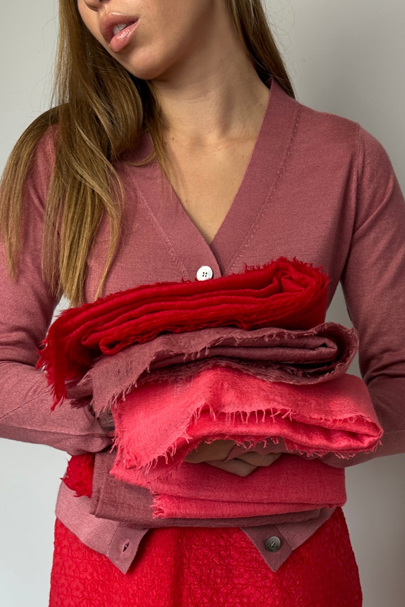 Woman holding folded red and pink fabric against a plain background