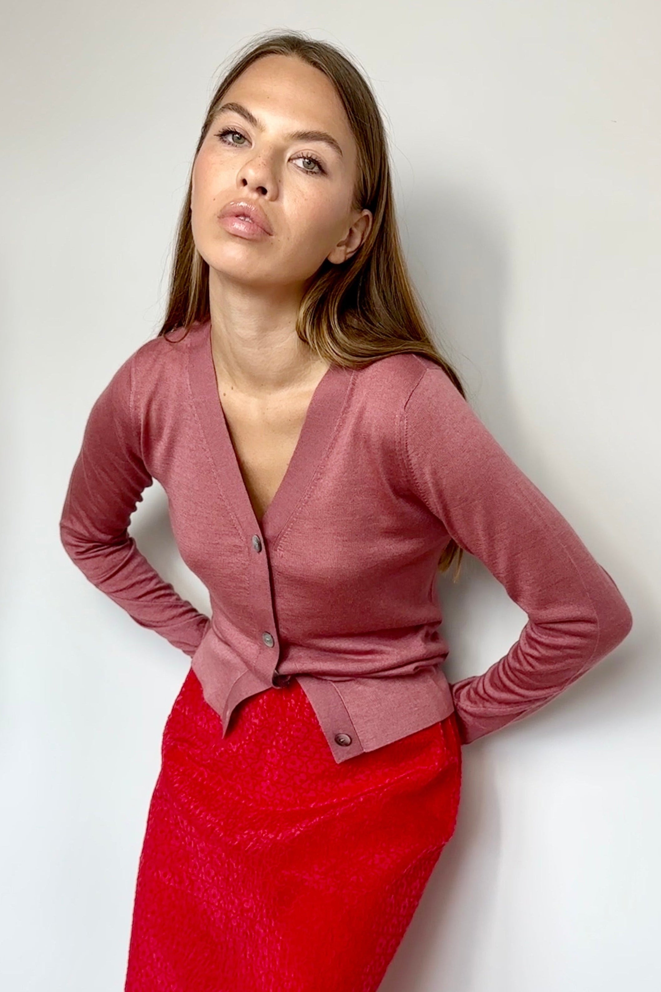 Woman wearing a pink cardigan and red skirt against a white background