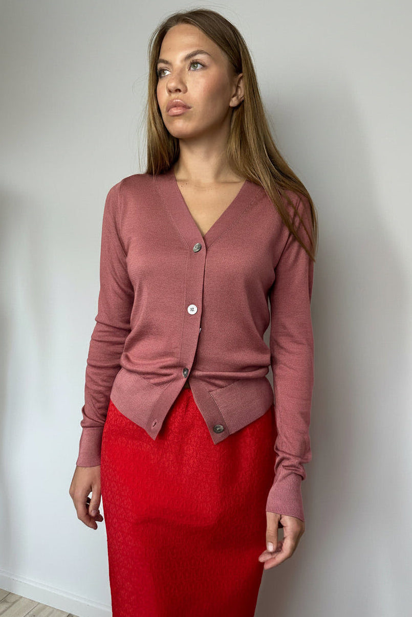 Woman wearing a pink cardigan and red skirt against a white wall.